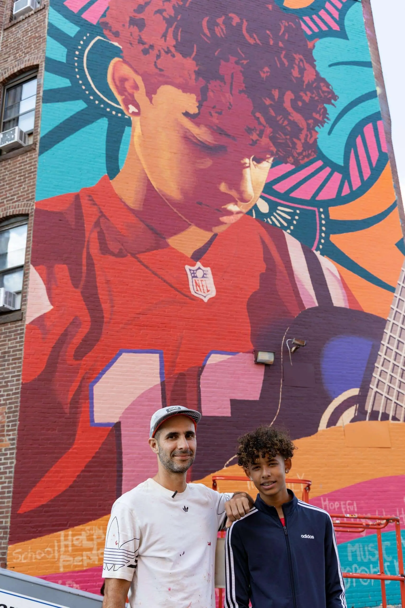 two men standing in front of a large mural.