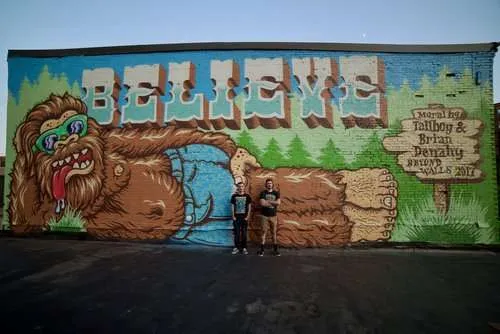 two people standing in front of a large mural.