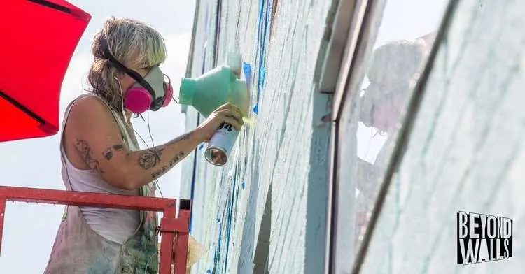 a woman wearing a mask spray painting a wall.