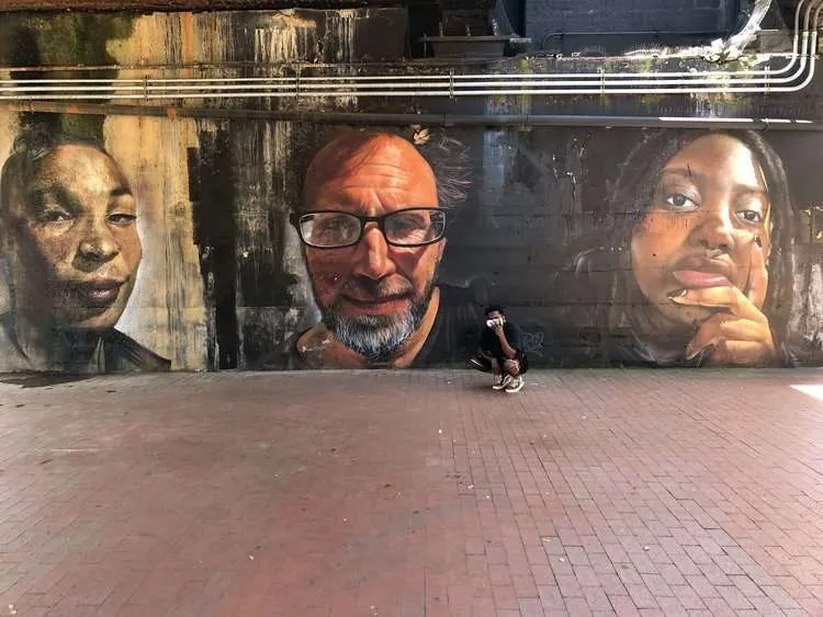 a person standing in front of a wall with a mural of people on it.