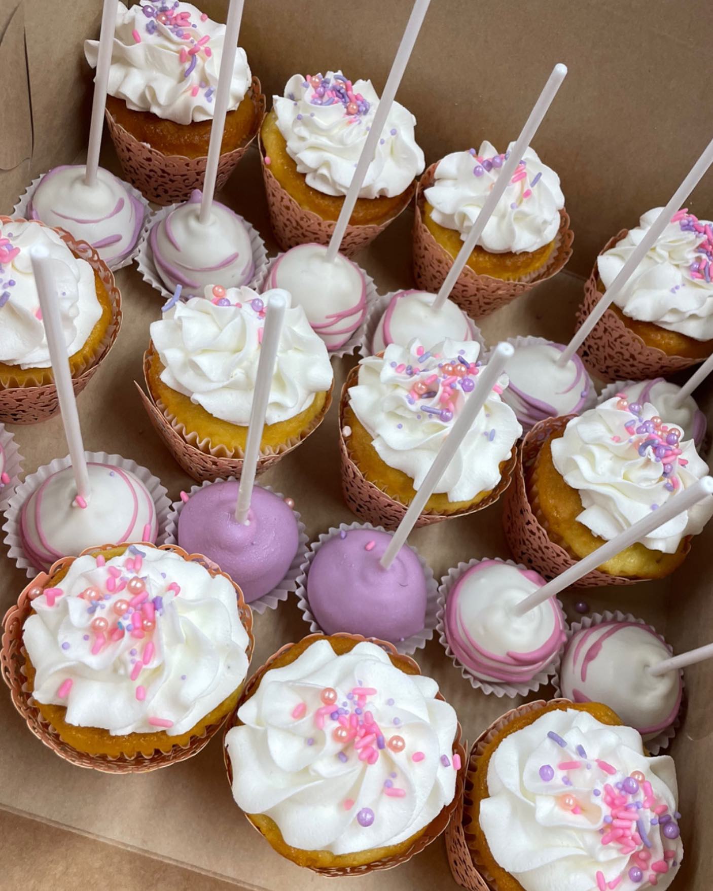 a box full of cupcakes with white frosting and sprinkles.