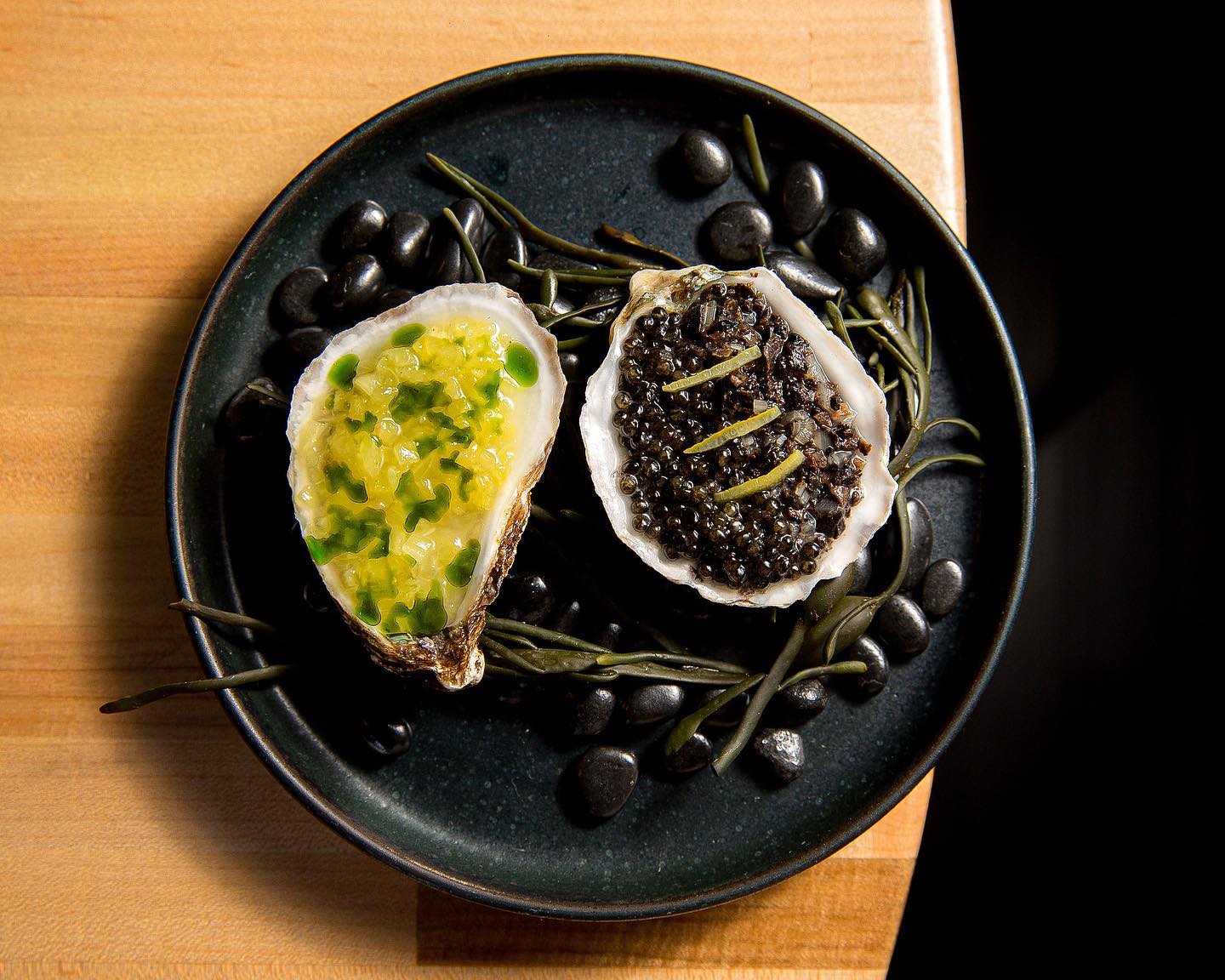 a black plate topped with an open oyster and black olives.