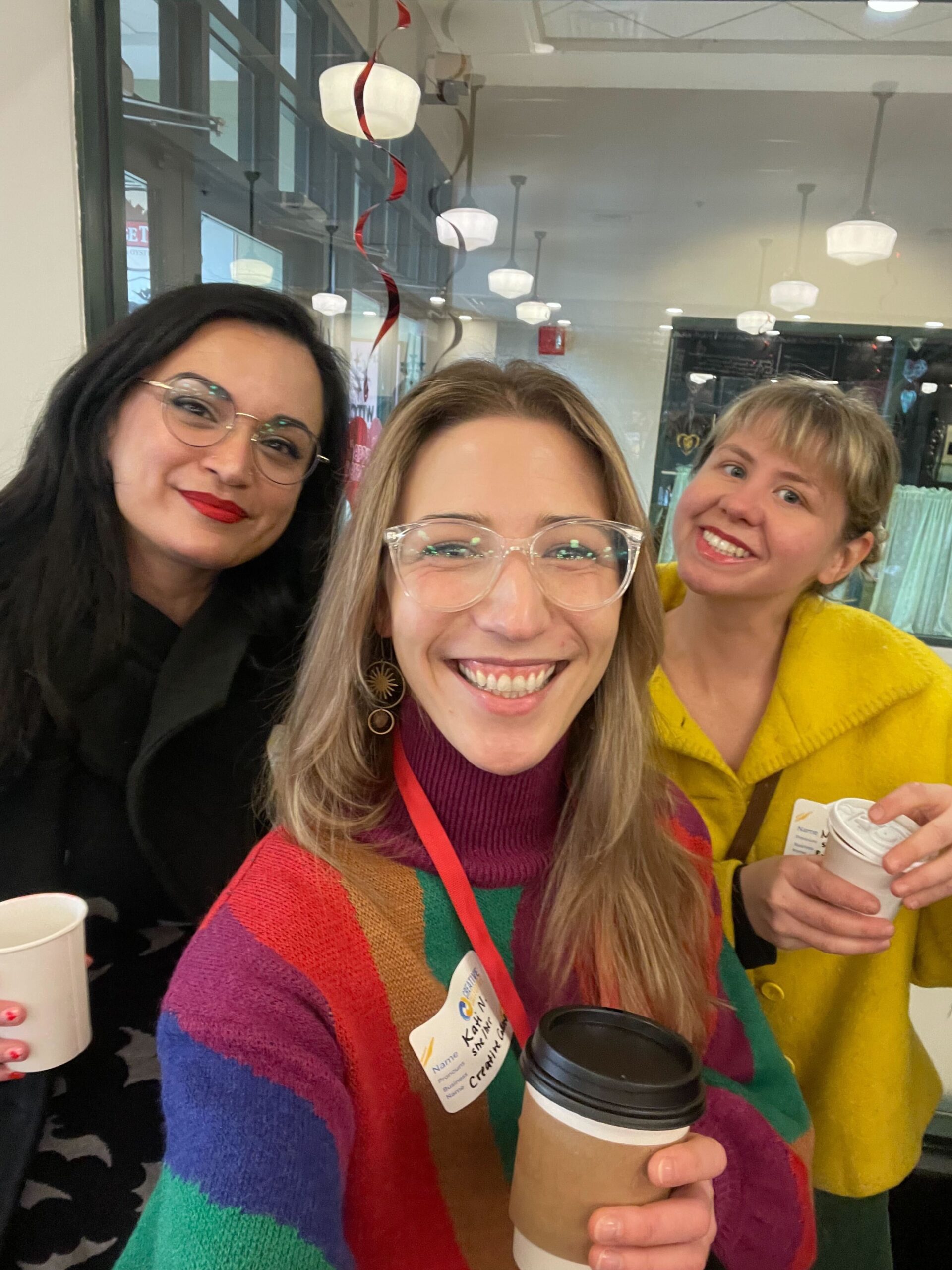 three women holding coffee cups and smiling for the camera.