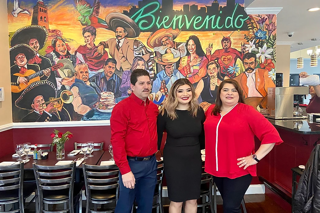 three people standing in front of a mural in a restaurant.