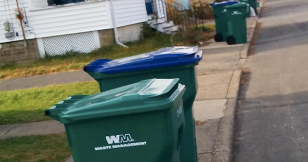 a couple of green trash cans sitting on the side of a road.