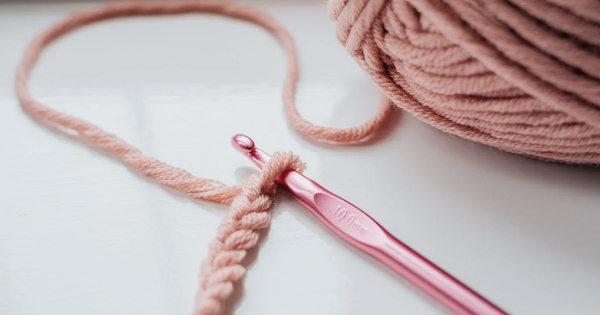 a pink crochet hook next to a ball of yarn.