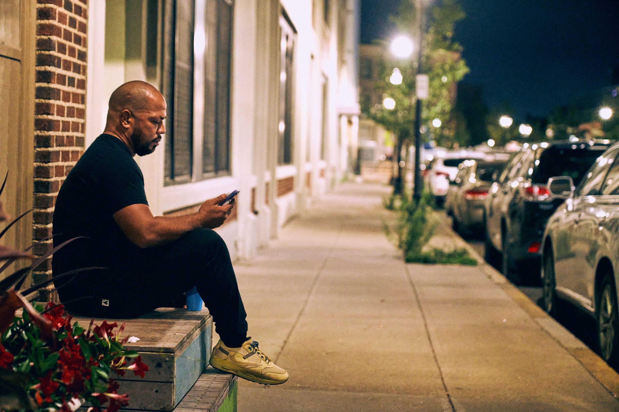 A man sitting on a sidewalk looking at his phone.