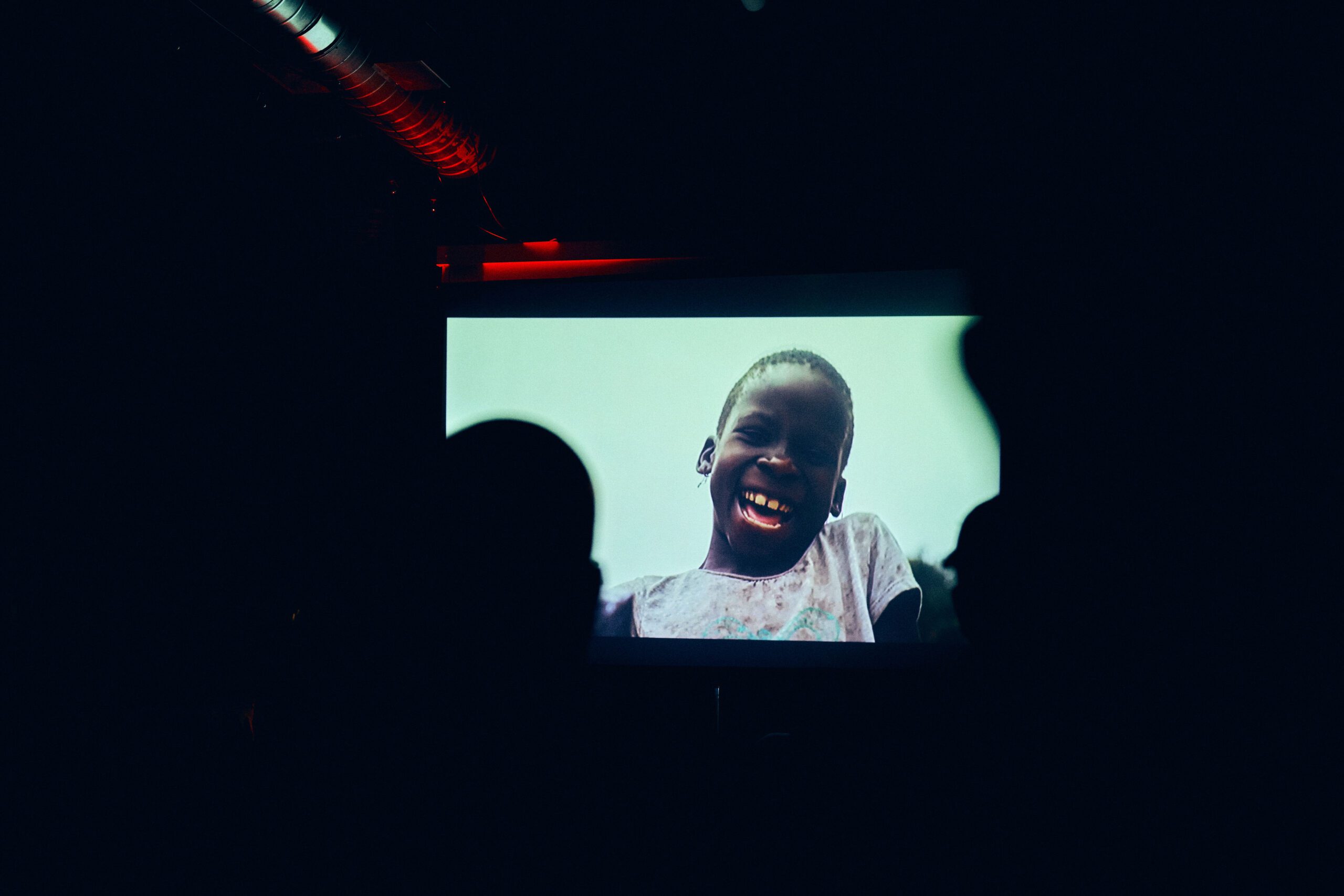 A child's face is shown on a screen in a dark room.