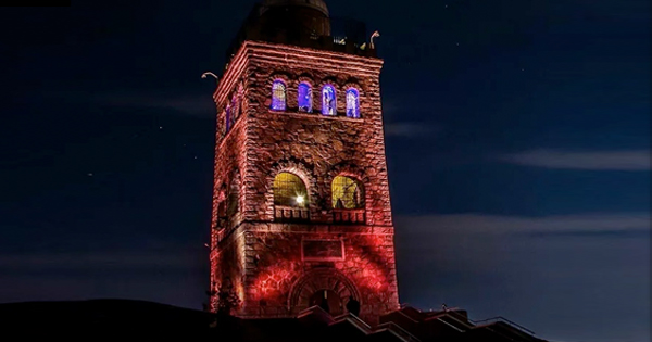 Explore the stunning beauty of a stone tower lit up with vibrant red and blue lights against the night sky.