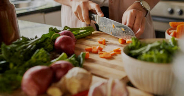 Capture the essence of fresh cooking with vibrant imagery: a person skillfully chopping carrots on a rustic wooden cutting board, surrounded by an enticing array of colorful vegetables, like red onions and leafy greens. This kitchen setting is alive with the promise of delicious creations.