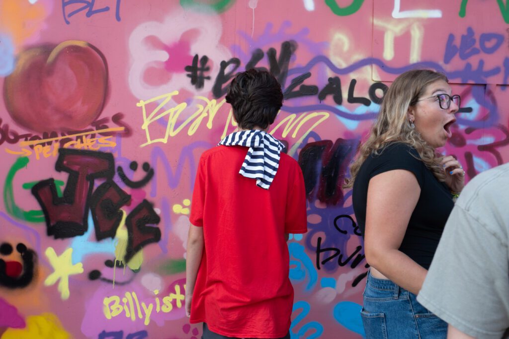 Two people connect with vibrant Essex County art—one admiring a lively graffiti wall, another reacting in joyful surprise nearby.