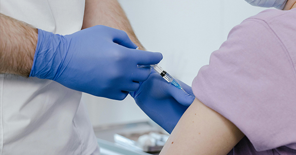 A healthcare worker in blue gloves brings community care to life, giving a vaccine in Essex County to someone in a purple shirt.