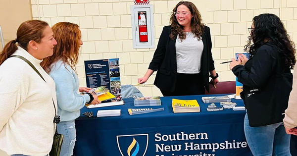 Four women connect at a lively SNHU table, exchanging ideas and smiles while sharing resources that inspire the Essex County community.