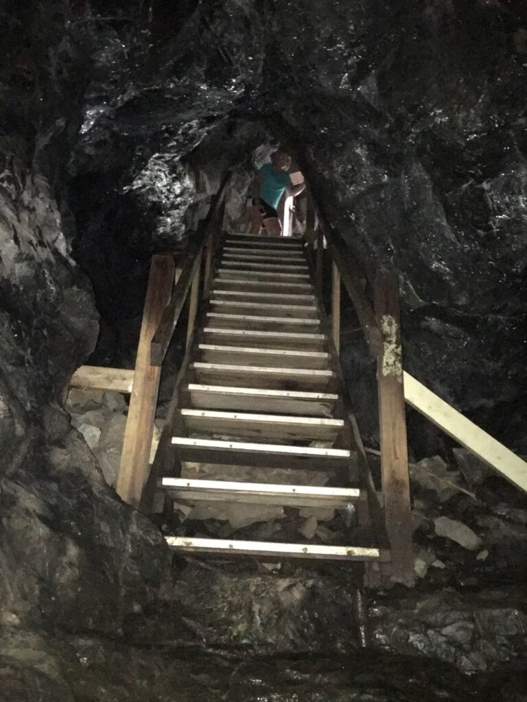 A wooden staircase ascends inside a dramatic cave as two community members, aglow in light, connect at Essex County’s inspiring summit.