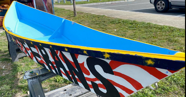 A vibrant boat with blue and yellow details showcases stars and stripes like the American flag, uniting Essex County spirit on its trailer.