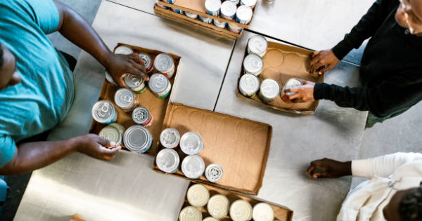 Three community members join forces, hands busy organizing canned goods into boxes for Essex County, captured in a vibrant overhead shot.