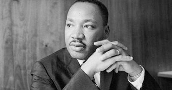 A thoughtful man in a suit, mustache and short hair, sits poised against wood paneling—reflecting Essex County’s creative spirit.
