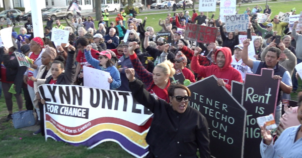A spirited crowd rallies in Essex County, waving creative signs and a "Lynn United for Change" banner, fists raised in unity.