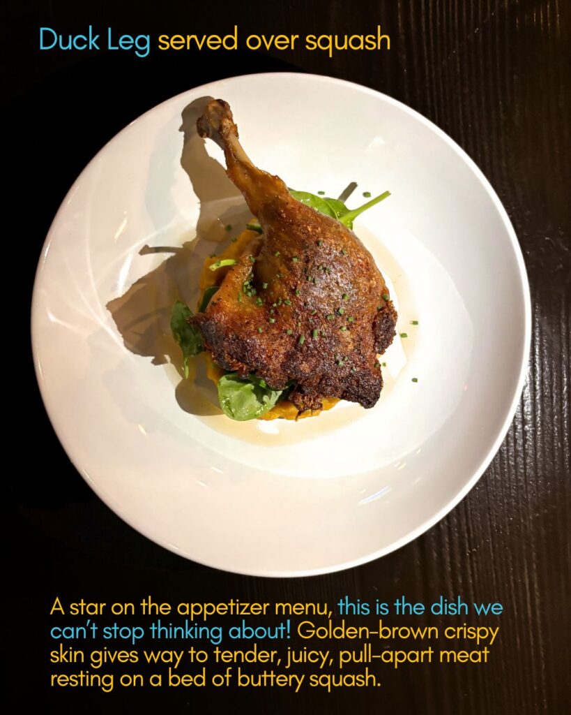 A cooked duck leg with crispy brown skin is served on a mound of bright yellow squash in a white bowl, garnished with herbs. The bowl sits on a dark wooden table, and the image includes descriptive text about the dish.
