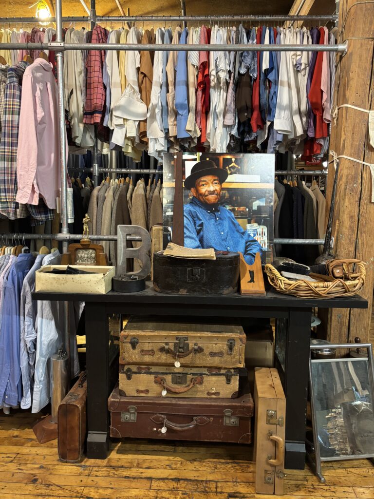 Display of vintage leather suitcases, framed portrait of Bobby Garnett, and clothing racks at Bobby from Boston in Lynn Vintage Warehouse in Downtown Lynn MA