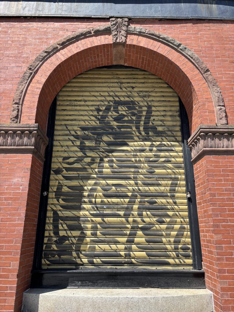 Brick archway on the exterior building of Lynn Vintage Warehouse at 545 Washington St in Lynn MA with a painted mural by IMAGINE (aka Sneha Shrestha), a Nepali artist who paints in her native language and meshes the aesthetics of Sanskrit scriptures with graffiti influences